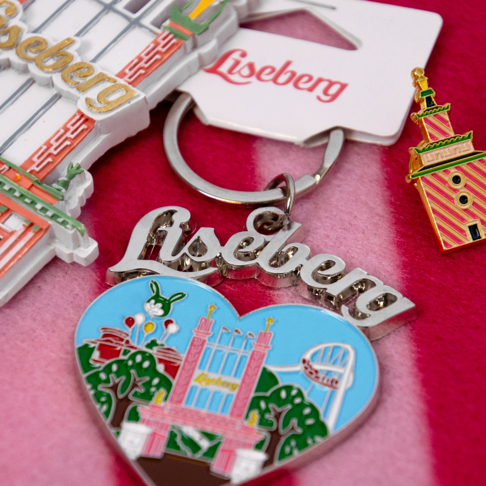 Färgglada Liseberg-souvenirer, inklusive nyckelringar och ett hjärtformat märke, ligger samlade på ett rosa tyg.