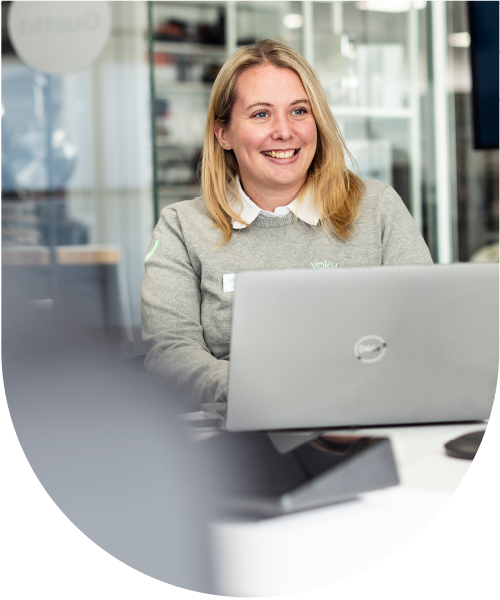 Kvinnlig Voky-anställd sitter vid ett skrivbord med en dator och ler